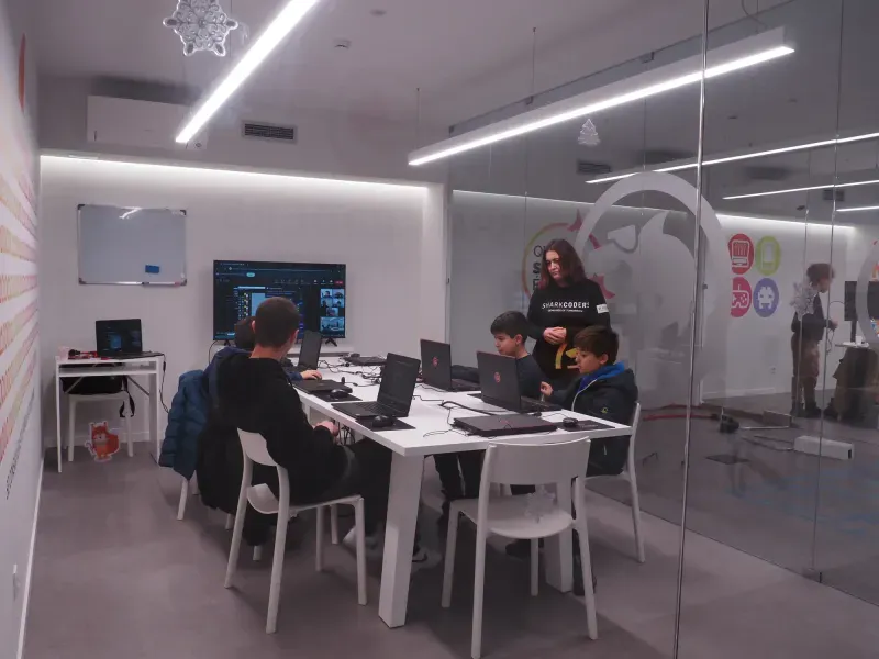 Profesora con sudadera SHARKCODERS en el aula, con alumnos programando